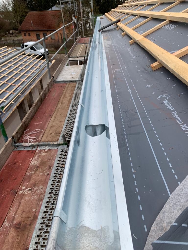 Dachaufbau auf Baustelle: Metallrinne am Dachrand, Holzlatten und Gerüst sichtbar