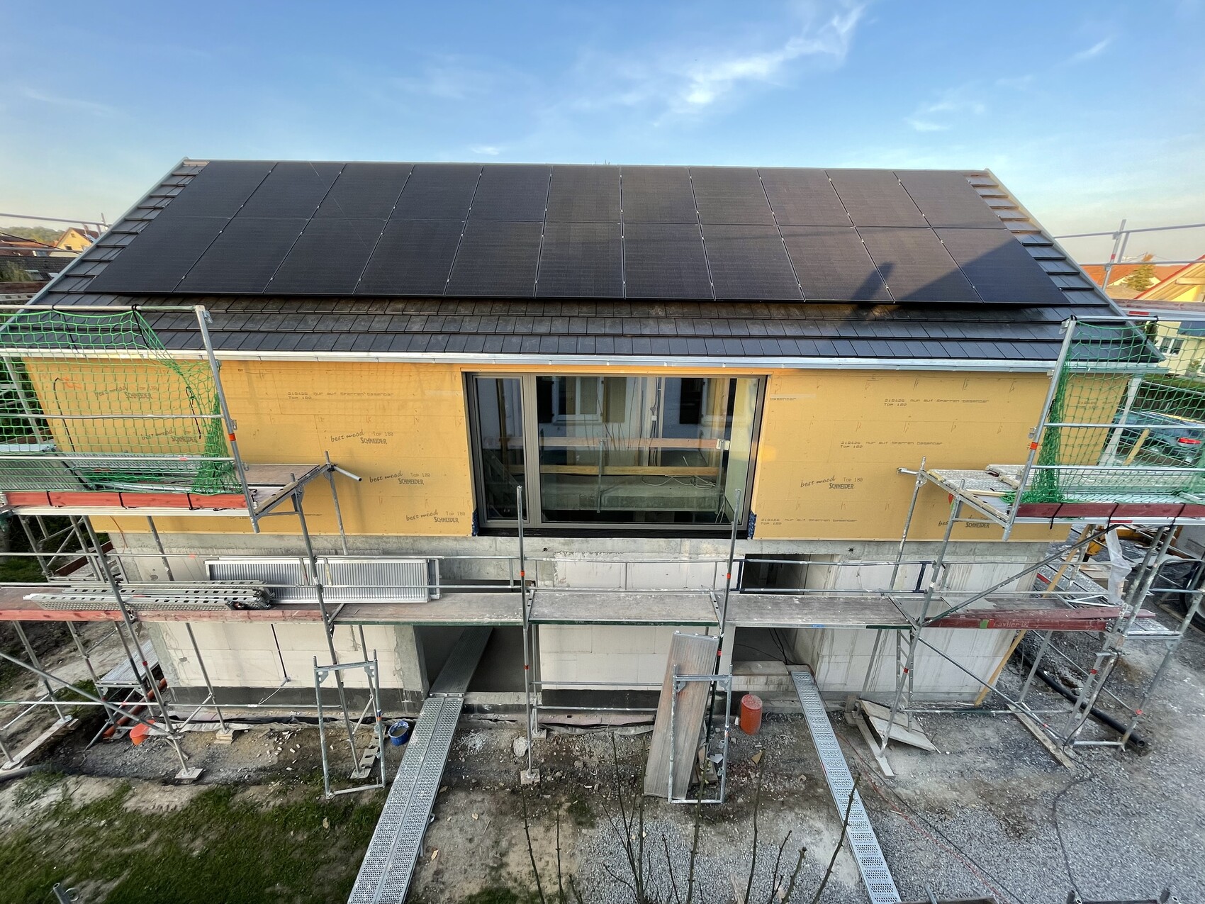 Dach eines Hauses mit installierten Solarpanelen; umlaufendes Baugerüst und Bauarbeiten sichtbar.