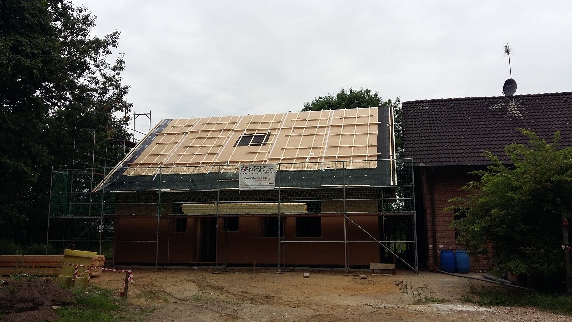 Einfamilienhaus im Rohbau: Holz-Dachkonstruktion, umlaufendes Gerüst, Baustelle vorne.