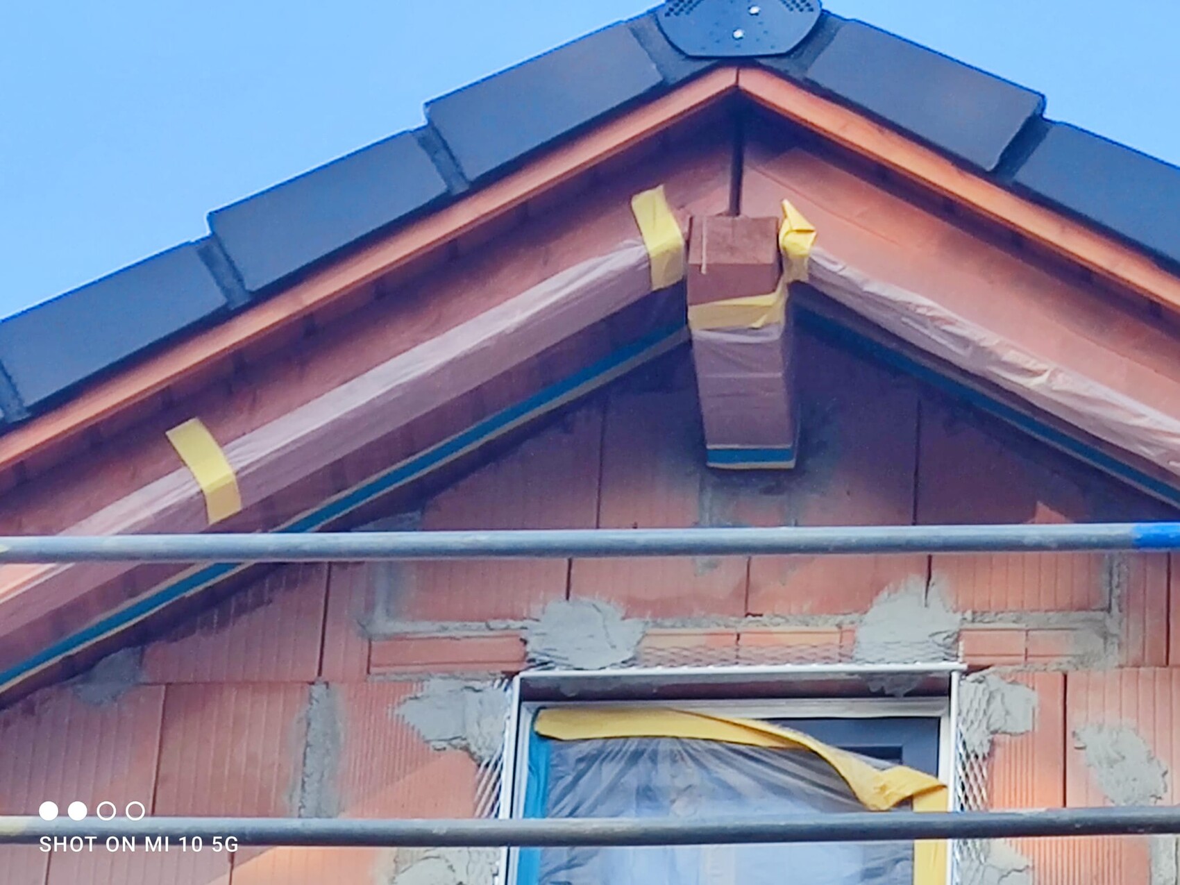 Dach eines Hauses im Bau mit Gerüststangen, Fensterfolie, gelbem Klebeband, blauem Himmel