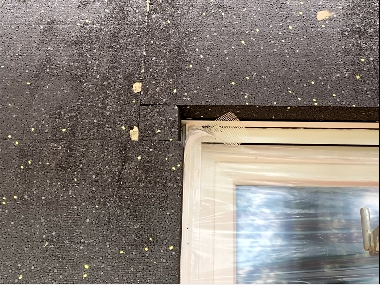 Fensterrahmen am Dach mit Schutzfolie, dunkle Dachfläche mit gelben Flecken.