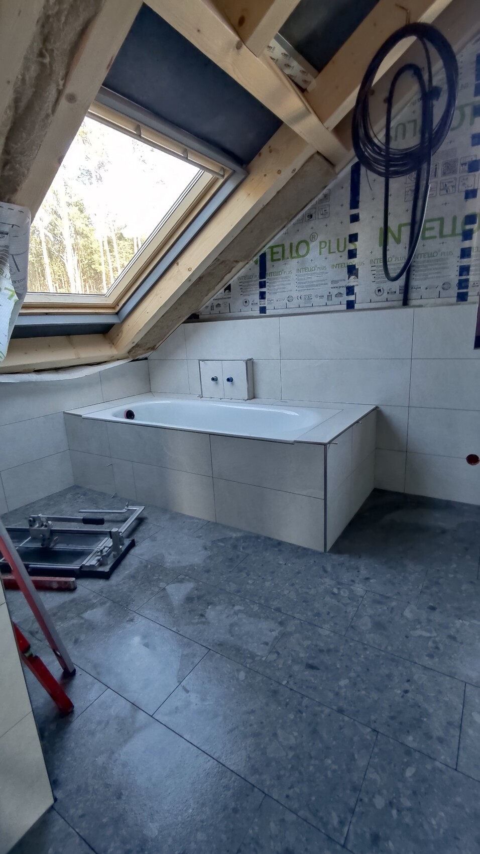 Badezimmer im Bau mit eingebauter Badewanne unter Schrägdachfenster, Dämmplatten und Werkzeugen.