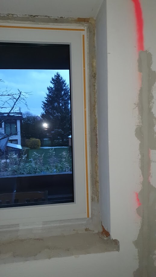 Neues Fenster im Baubereich, Wand verputzt; Außenbereich mit Baum und Garten sichtbar.