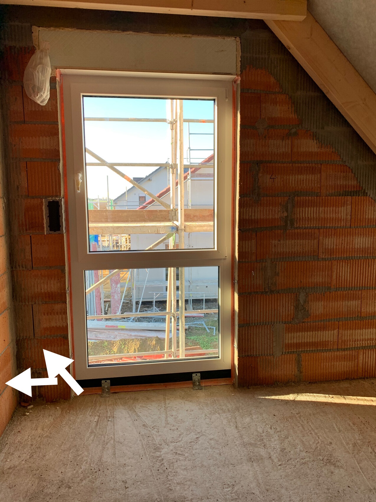 Fenster in einer unfertigen Wand; Baustellengerüst draußen sichtbar und Bauarbeiten erkennbar.