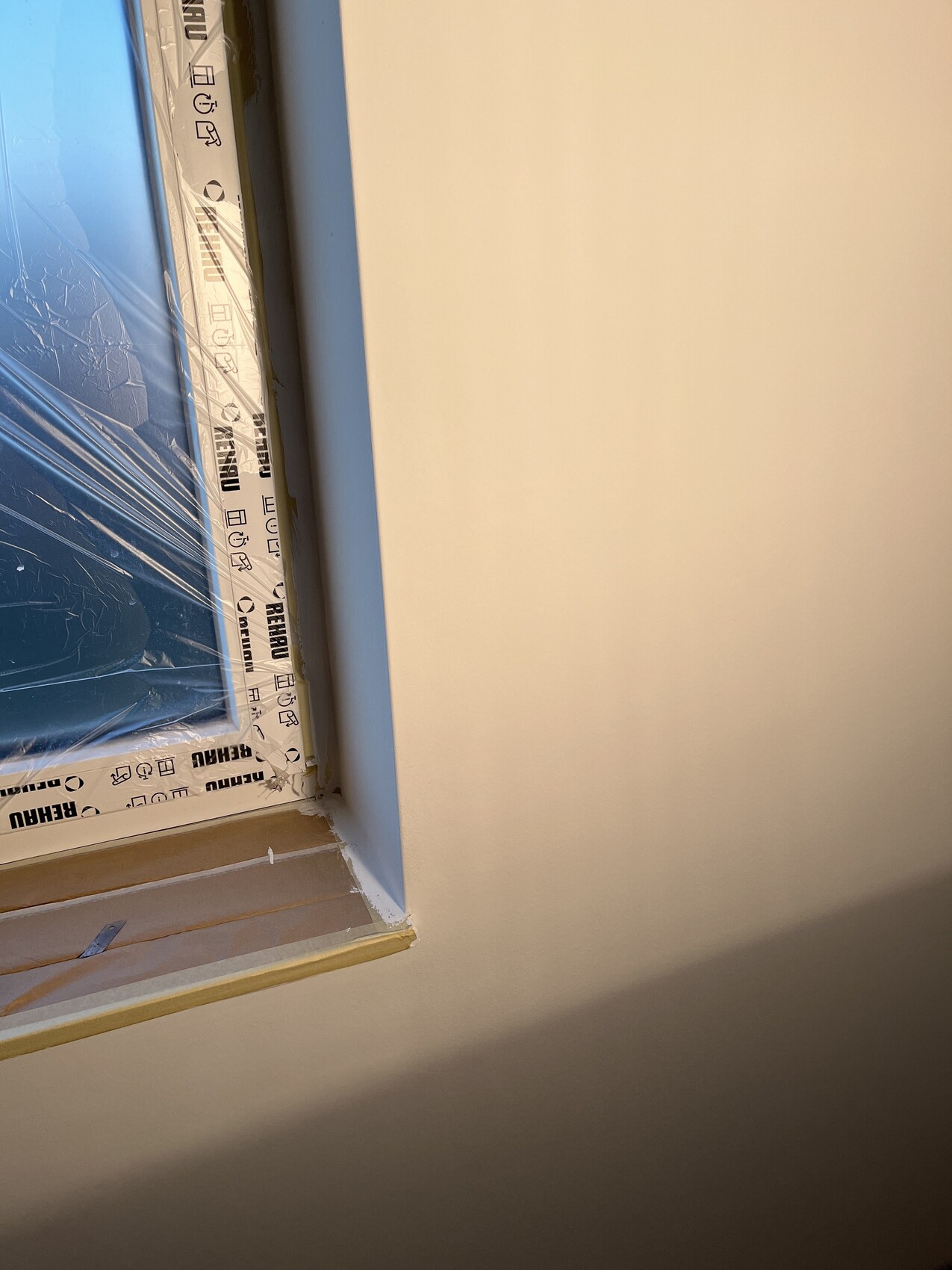 Fensterrahmen mit Schutzfolie und Klebeband, beige Wand rechts, Innenausbau im Gange.