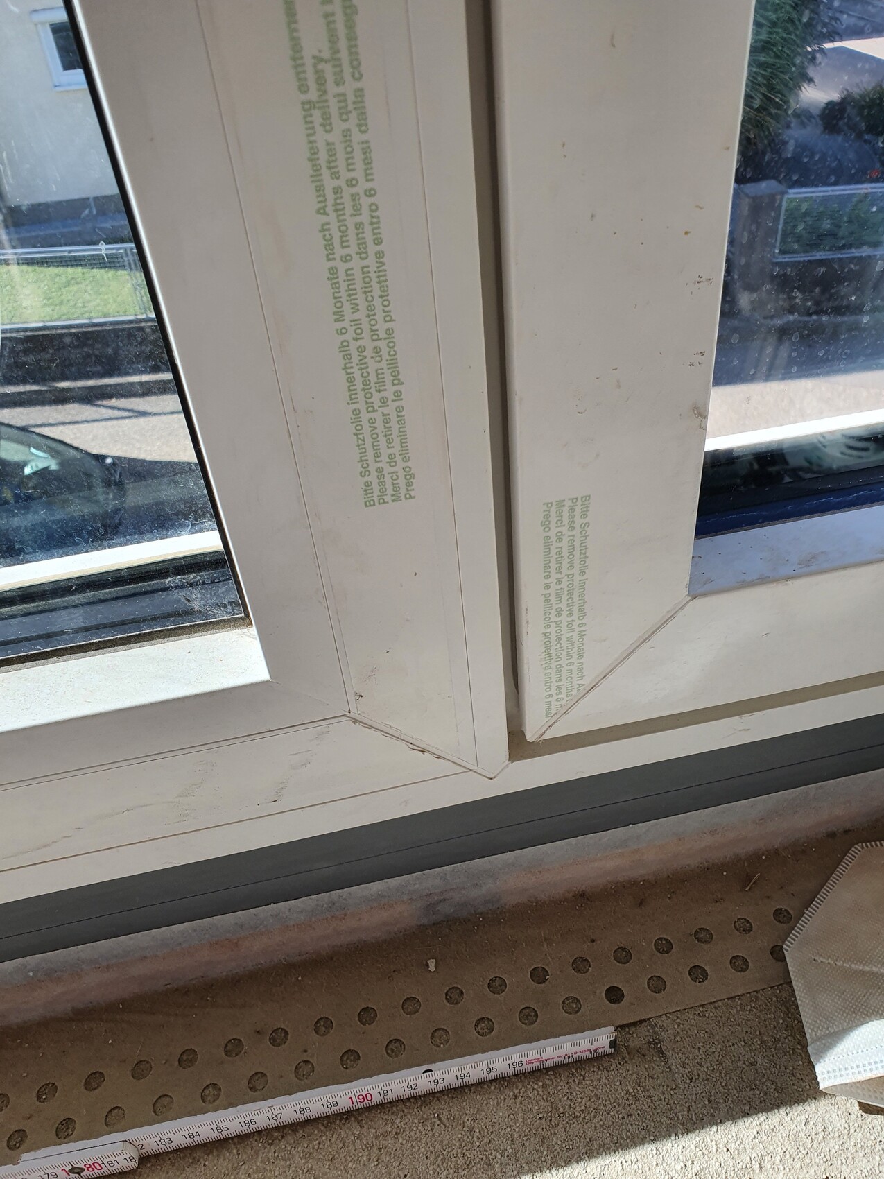Weißer Kunststoff-Fensterrahmen mit grünem Schutztext; Maßband liegt am Boden.