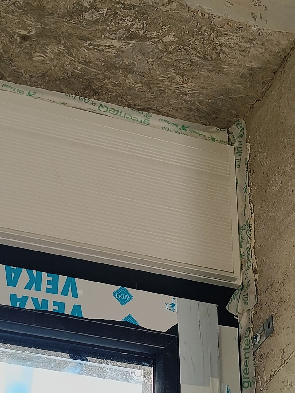 Weißer Rollladen im Fensterrahmen, Baufolie um das Fenster, rauer Rohbau.