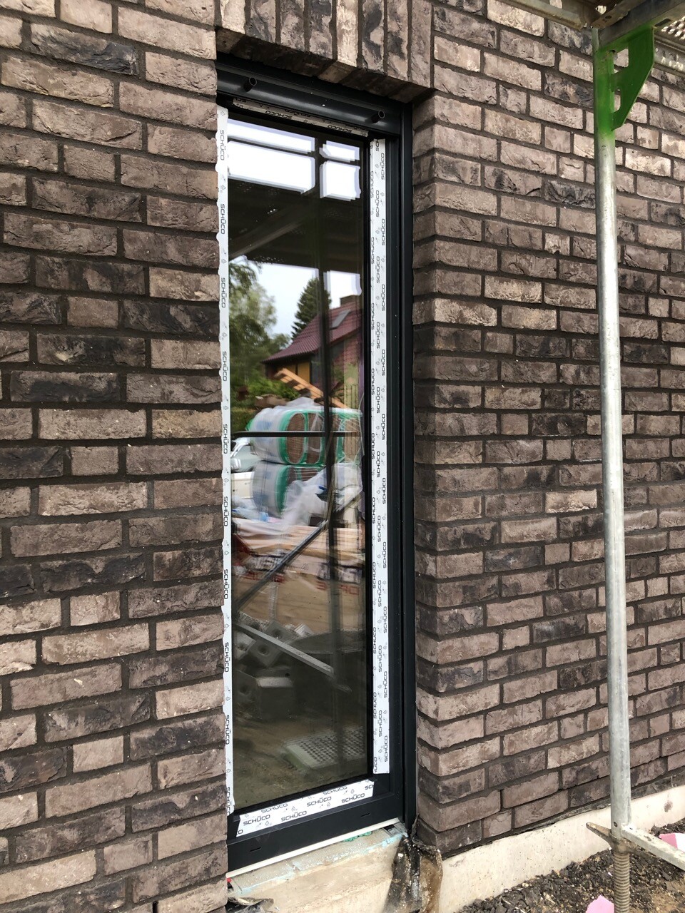 Neues Fenster mit schwarzem Rahmen in Ziegelwand, Schutzband, Baugerüst rechts.