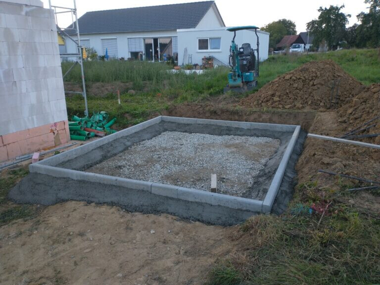 Neues Fundament wird auf einer Baugrube für ein Haus gelegt; Baugerät im Hintergrund