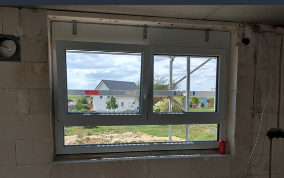 Doppel-Fenster in unfertiger Wand; Außenblick auf Haus, Garten und Baugerüst.