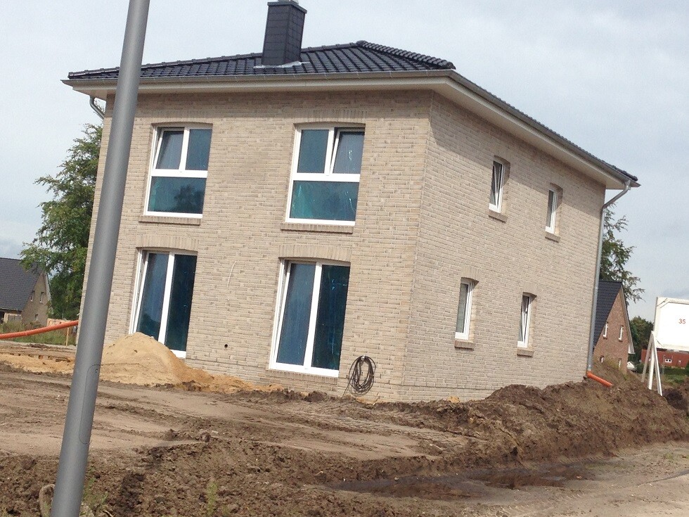 Neues zweistöckiges Ziegelhaus im Bau, große Fensterfront, Baugrund mit Erdarbeiten.