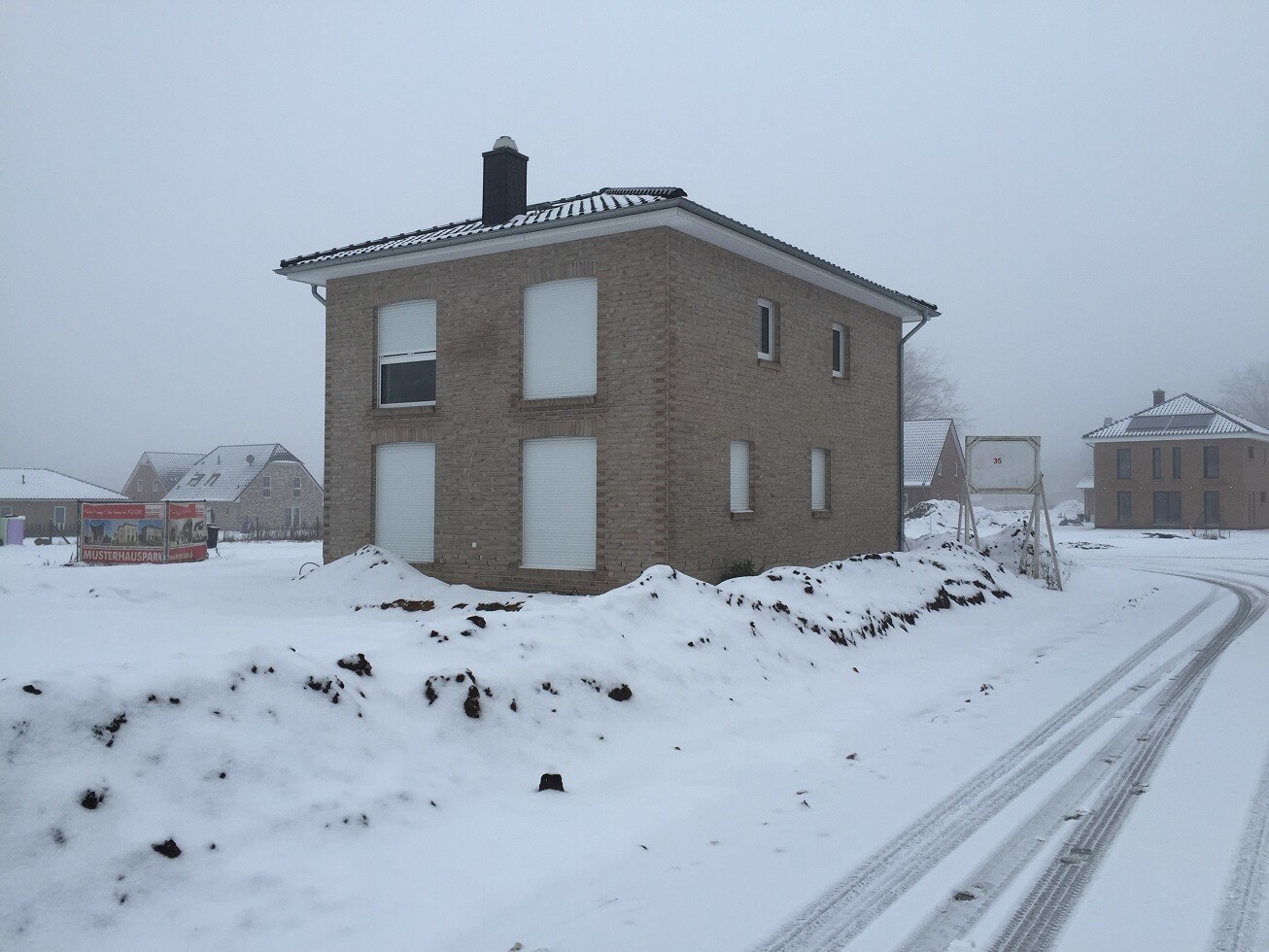 Zweistöckiges braunes Backsteinhaus in verschneiter Wohngegend, Straße mit Schneespuren.