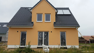 Zweistöckiges gelb-orangees Haus mit Satteldach, großen Fenstern und Terrassentür