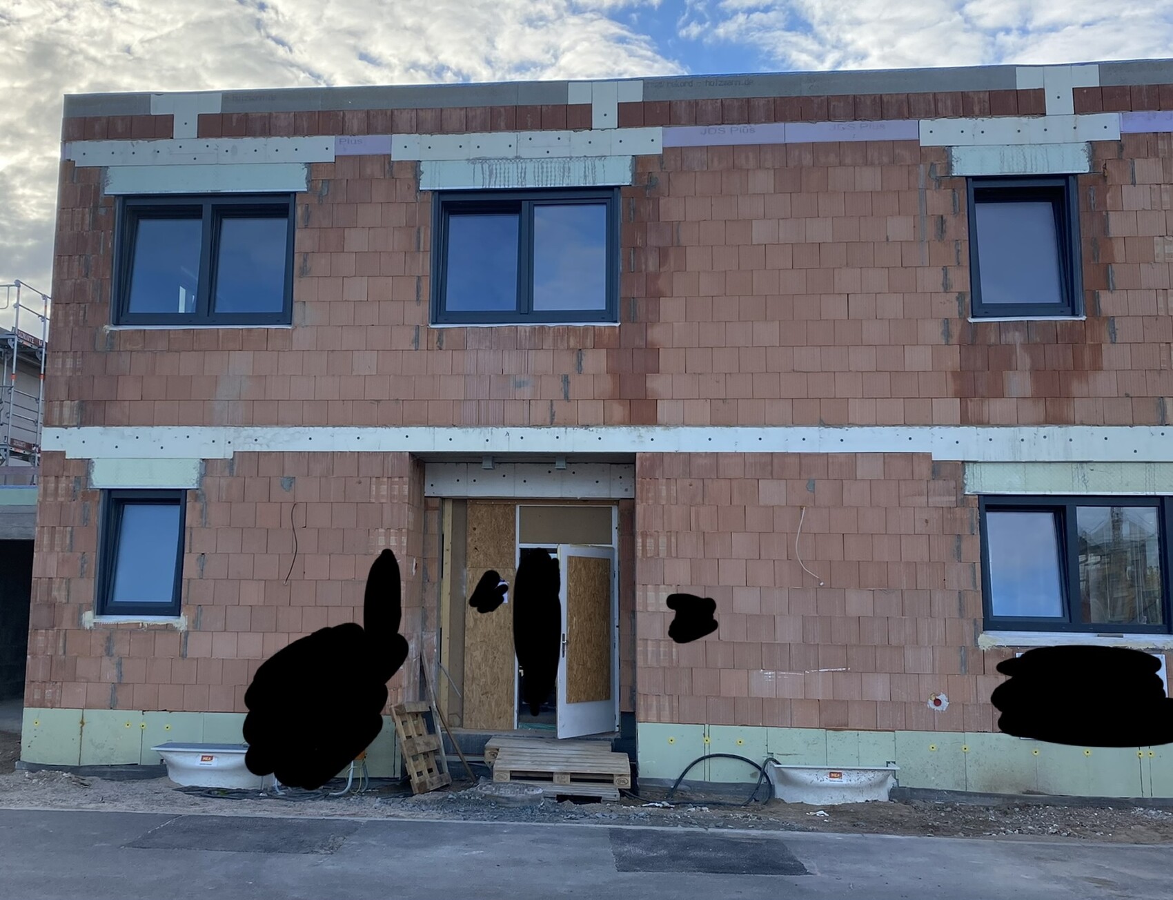 Zweistöckiger Rohbau aus roten Ziegeln mit dunklen Fensterrahmen, offener Eingang
