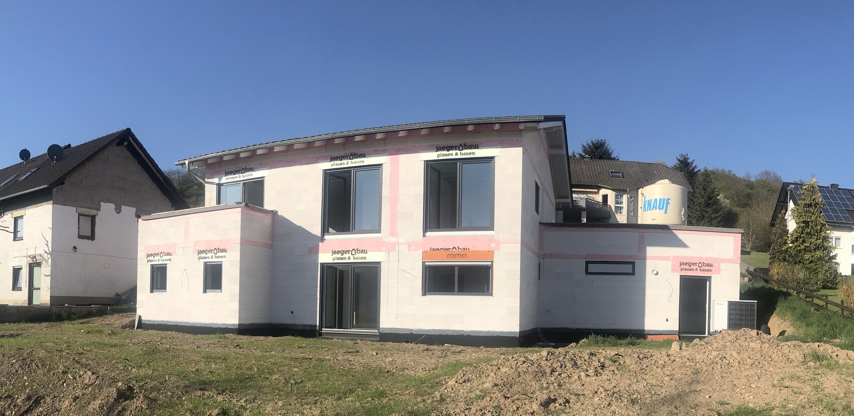 Neues zweistöckiges Haus auf Baustelle mit weißer Blockfassade, pinker Dämmung und großen Fenstern