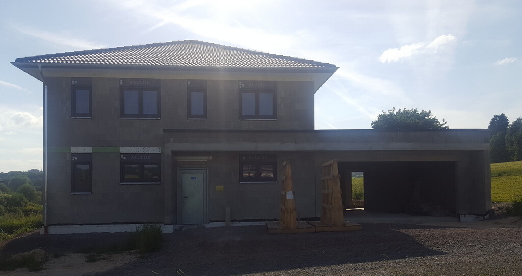 Zweistöckiges Neubauhaus im Bau, mit offener Garage und Baumaterialien davor auf dem Grundstück.
