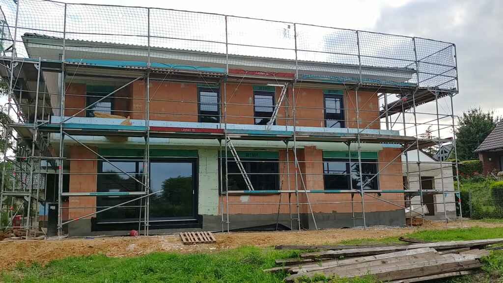 Zweistöckiges Haus im Bau mit Gerüst ringsum, orange Ziegelwände, große Glasfront