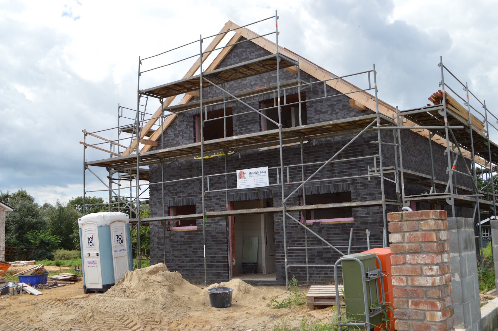 Zweistöckiges Haus im Bau mit dunklen Ziegeln und Gerüst.