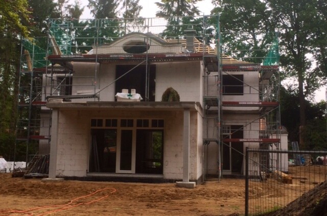 Zweistöckiges Haus im Rohbau mit Gerüst, Glasfronten und offener Baustelle.