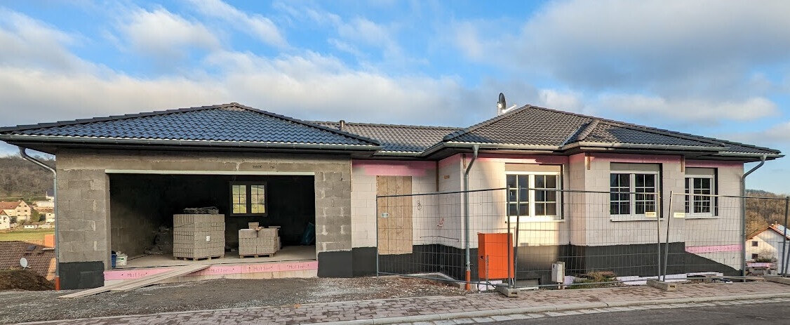 Neubau eines Einfamilienhauses mit Garage, Bauzaun und Baumaterialien auf der Baustelle.