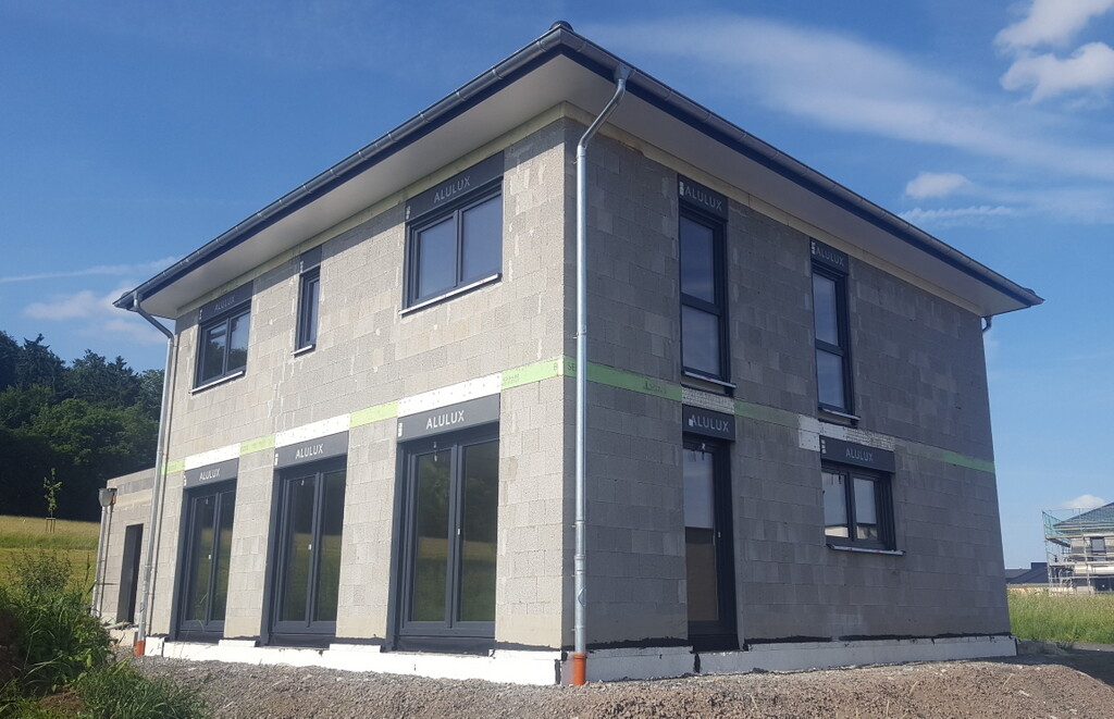 Zweistöckiges Rohbauhaus aus Betonblöcken mit großen Fenstern in Bauphase.