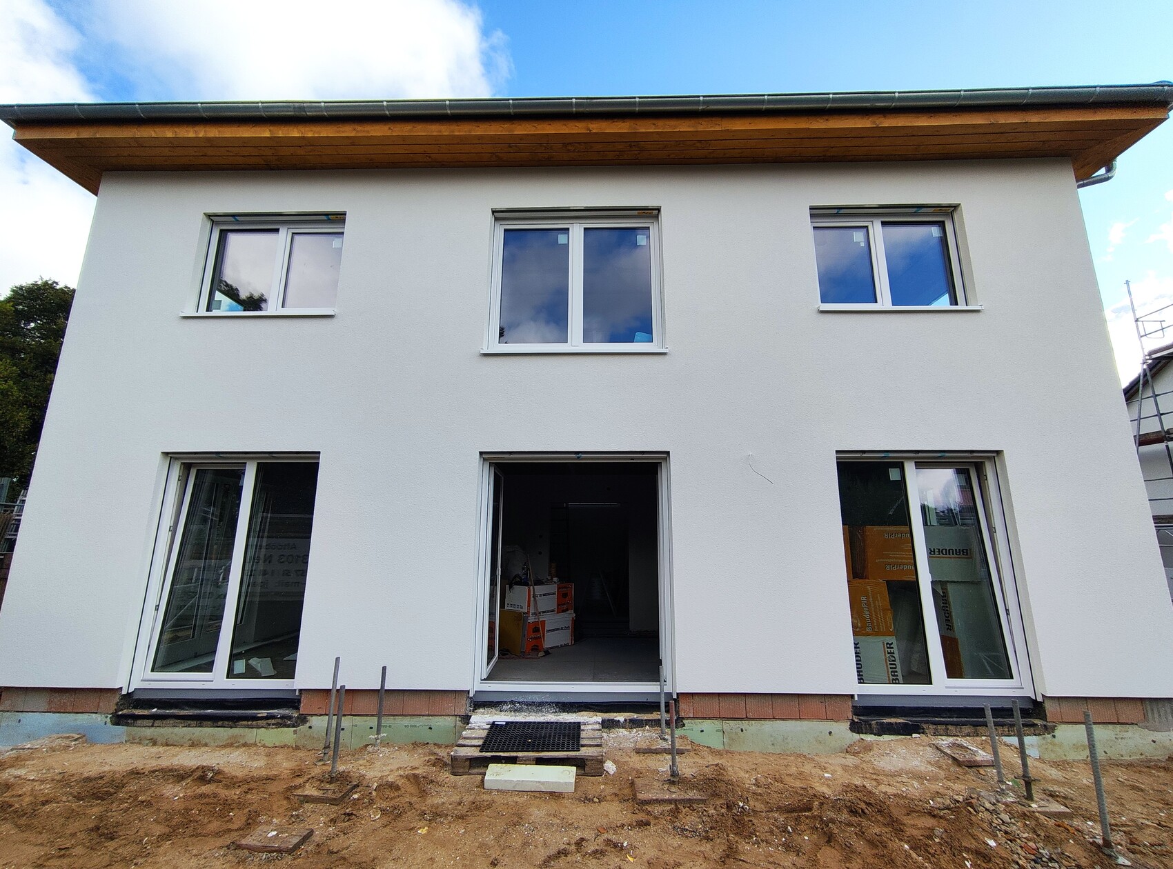 Weißes, zweigeschossiges Haus im Bau mit großen Fenstern, offener Eingangstür.