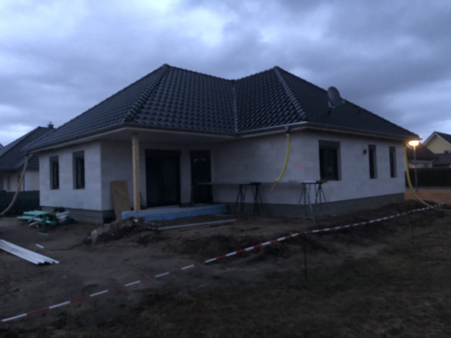 Einfamilienhaus im Rohbau mit dunklem Ziegeldach, Bauzubehör und Absperrband.