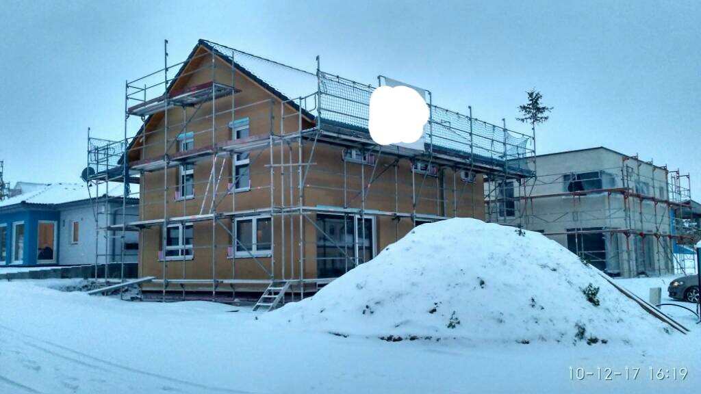 Zweistöckiges Haus mit Gerüst in verschneiter Wohnsiedlung; großer Schneehügel im Vordergrund.