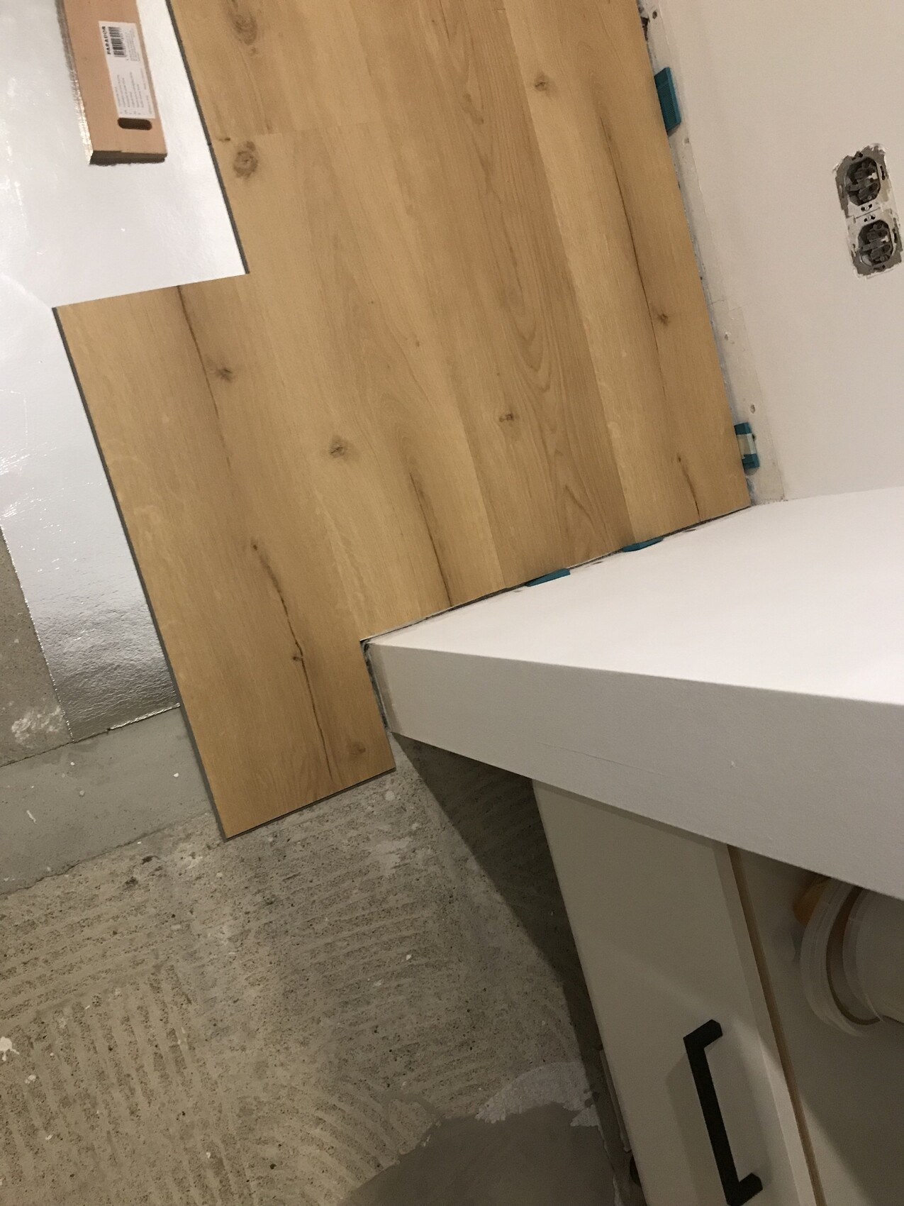 Holz-Laminatbodenplatten liegen auf dem Boden neben einem weißen Badezimmer-Schrank; offene Steckdosen.