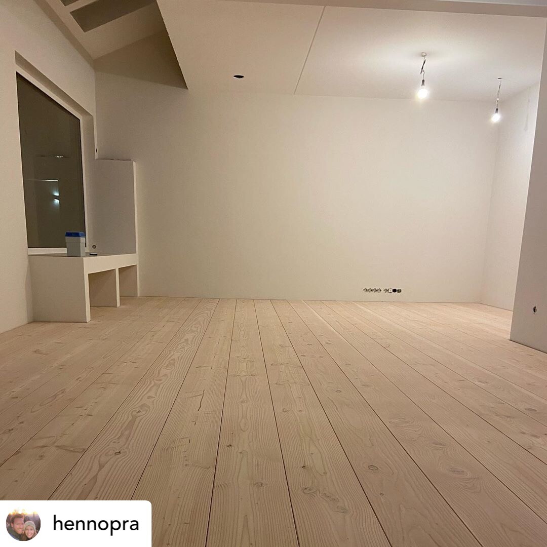 Leerer, heller Innenraum mit hellem Holzboden, Fenster links, zwei Glühbirnen.