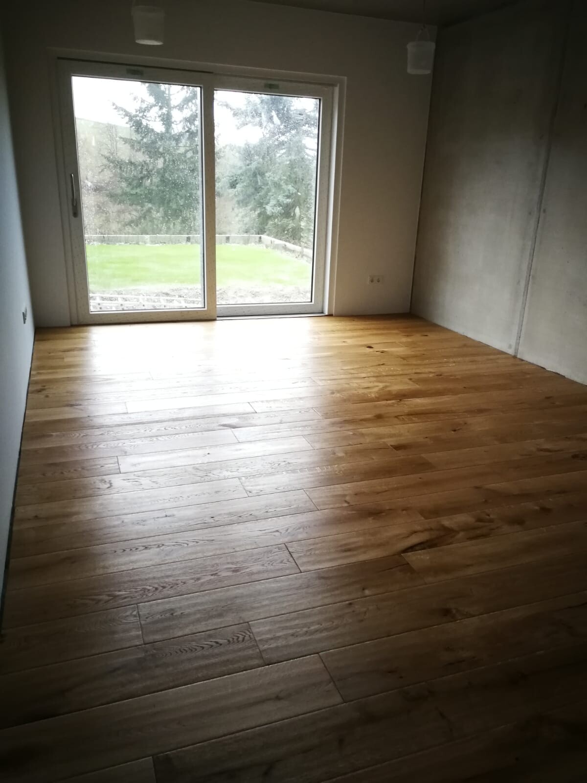 Leeres Zimmer mit Holzfußboden und großer Glas-Schiebetür zum Garten.