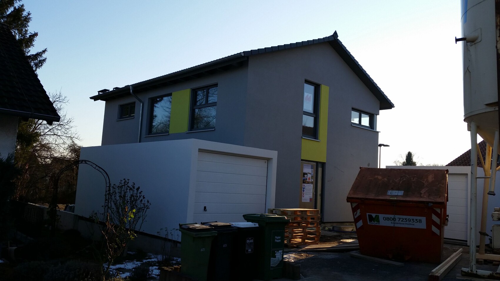 Modernes zweistöckiges Haus mit grauer Fassade, gelben Akzenten, Garage und Baustelle