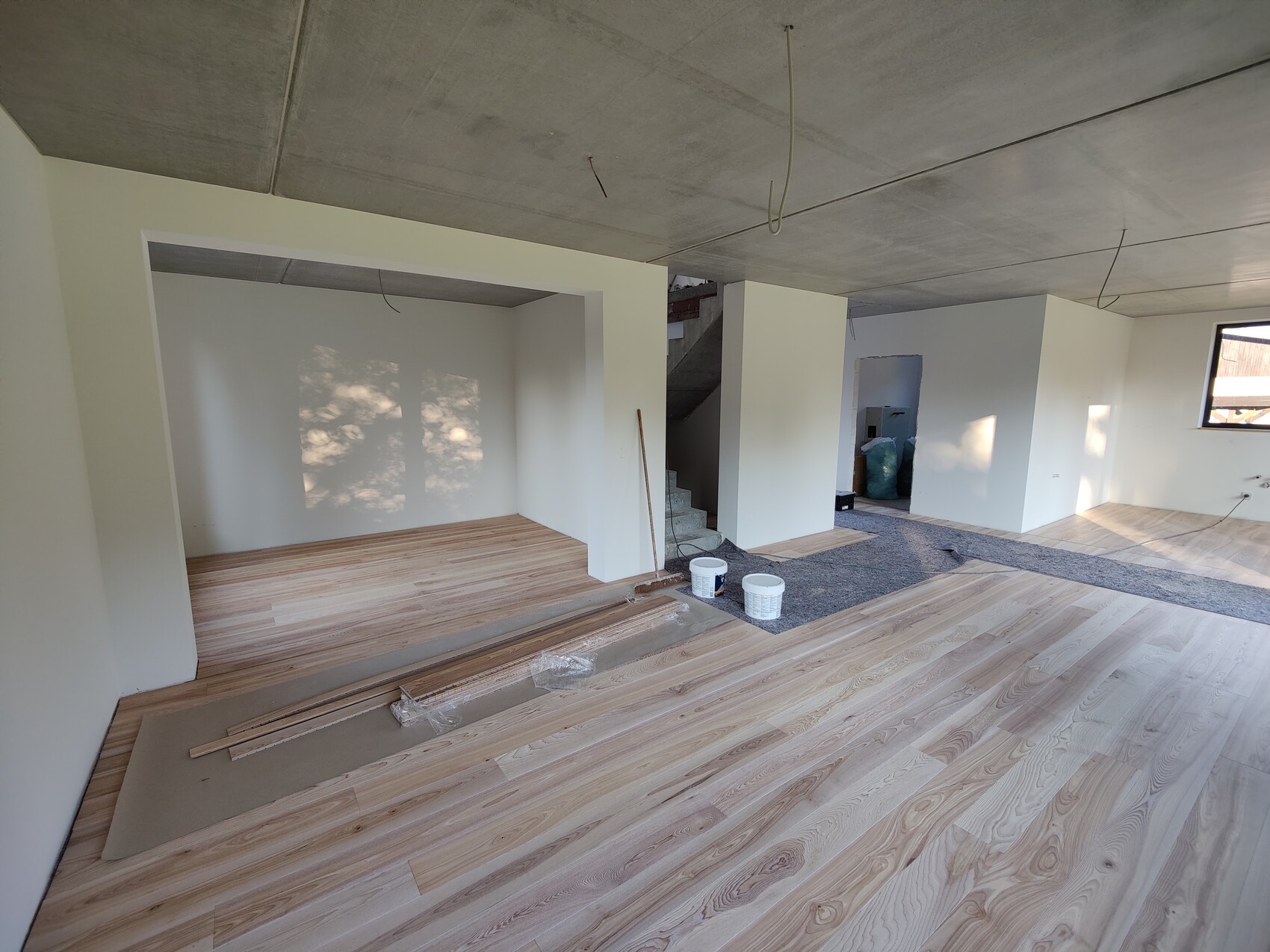 Offenes Renovierungswohnzimmer mit Holzfußboden, weißen Wänden, Treppe und Baumaterialien.