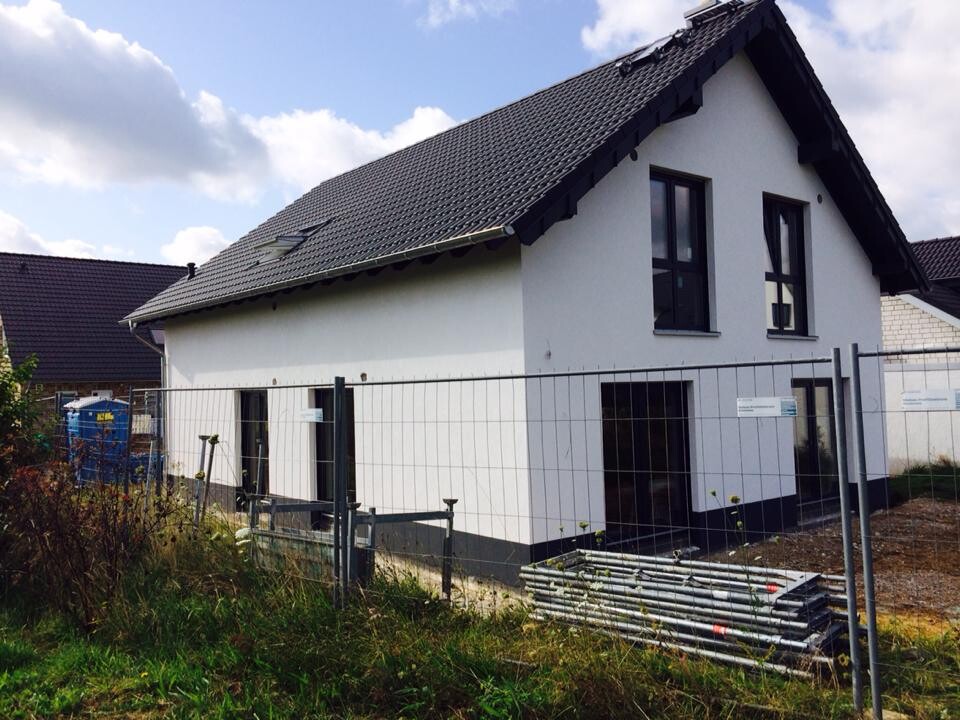 Neubau eines weißen Hauses mit dunklem Dach, Baustellenzaun und Baumaterialien