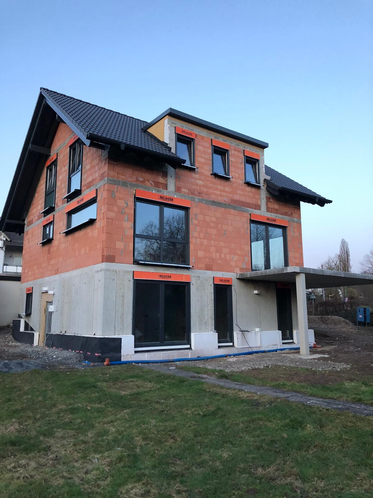 Neubau-Einfamilienhaus aus roten Ziegeln, große schwarze Fenster, Carport/Bodenplatte.
