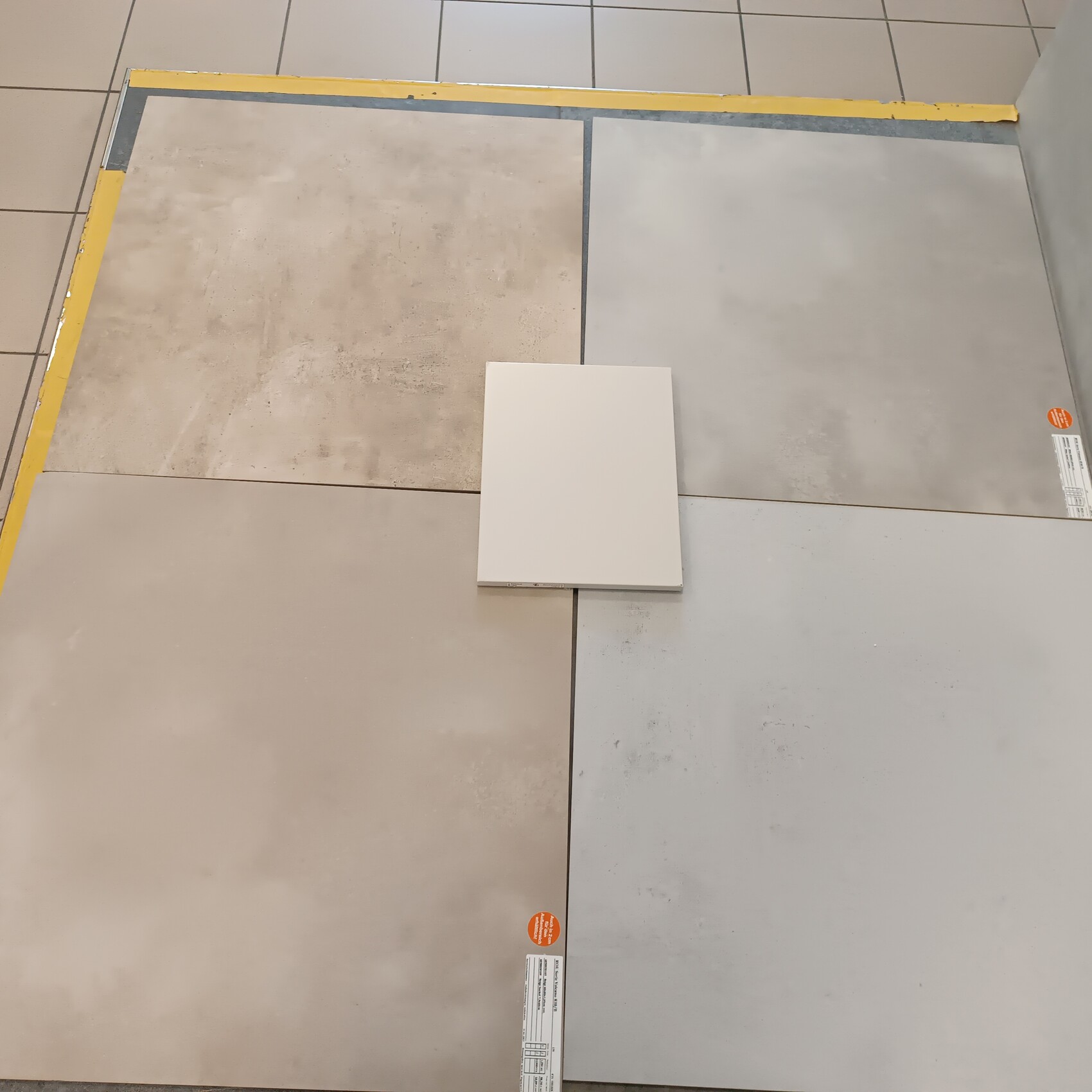 Übersichtsaufnahme von Bodenfliesen in Grau- und Beige-Tönen, zentrale weiße Quadratfliese.