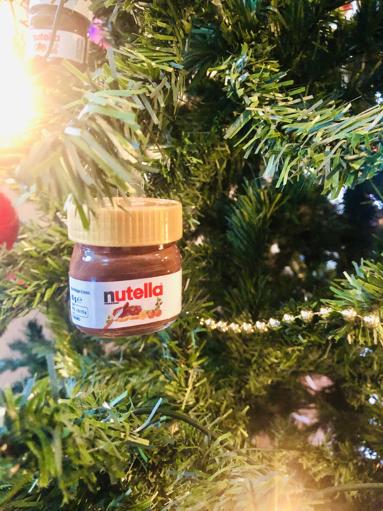 Kleines Nutella-Glas hängt an einem Weihnachtsbaum mit Lichterkette.