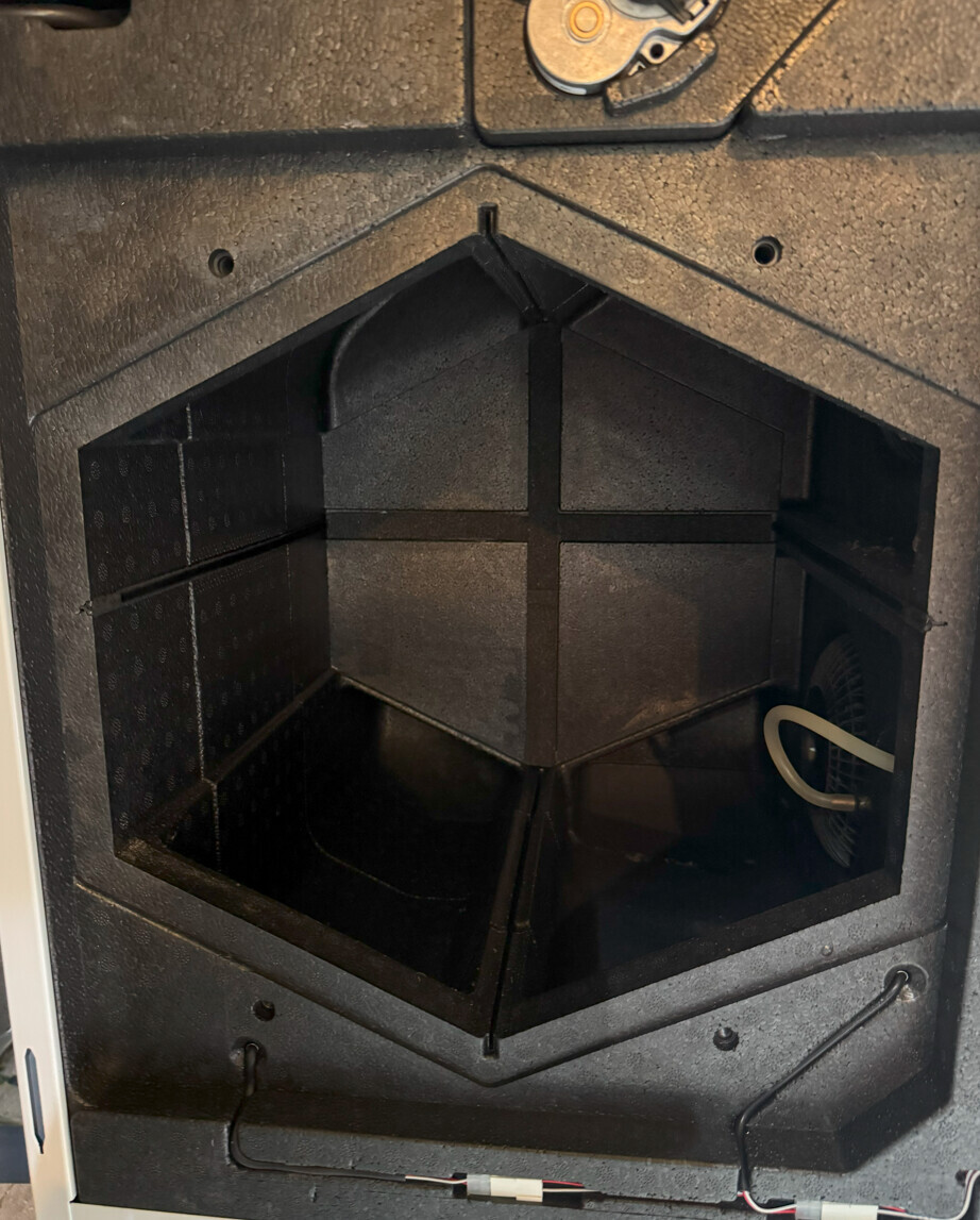 Innenansicht eines schwarzen Kamineinsatzes mit hexagonaler Kammer und Ascheboden.