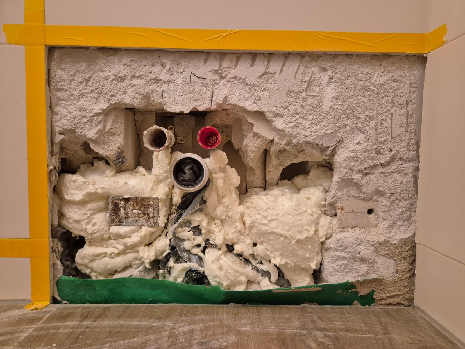 Offene Badezimmerwand mit sichtbaren Rohrverbindungen, Schaumisolierung und Baumaterial.