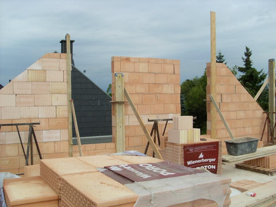 Baustelle mit unverputzten Ziegelwänden, Holzstützen, Kisten und Werkzeugen.