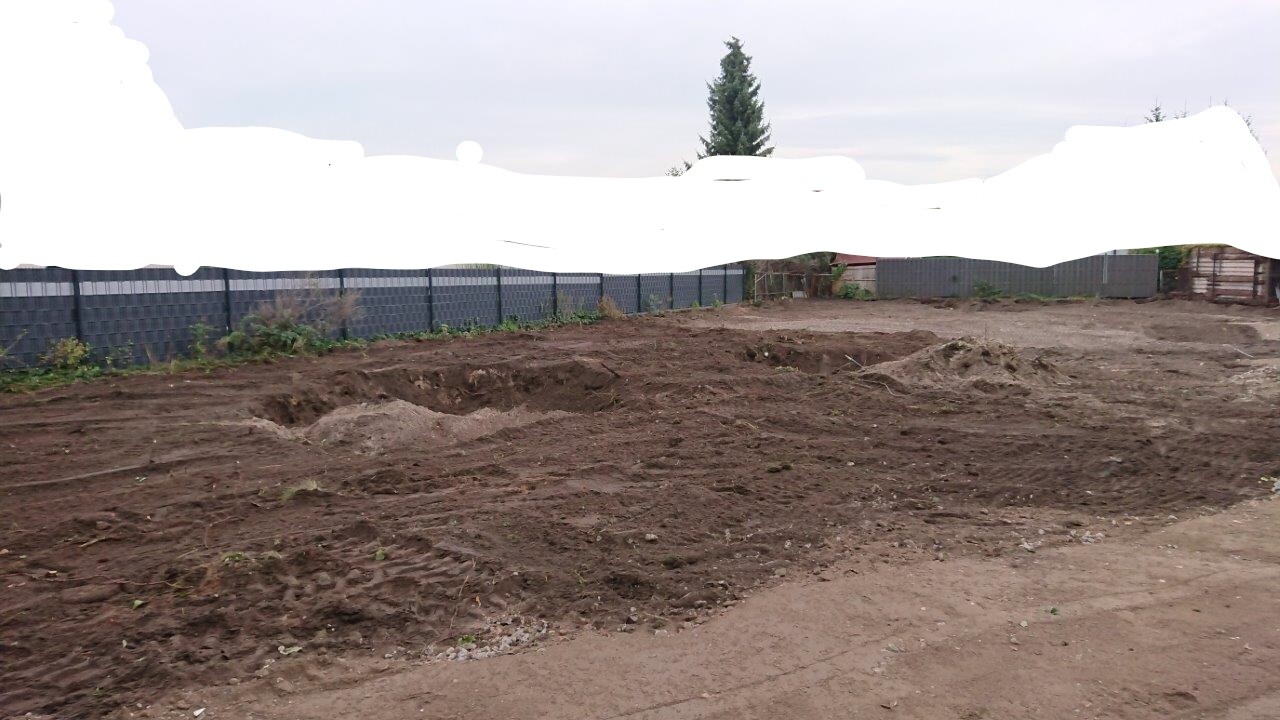 Baustelle im Garten: freigelegtes Erdreich, Gräben, Zäune im Hintergrund.