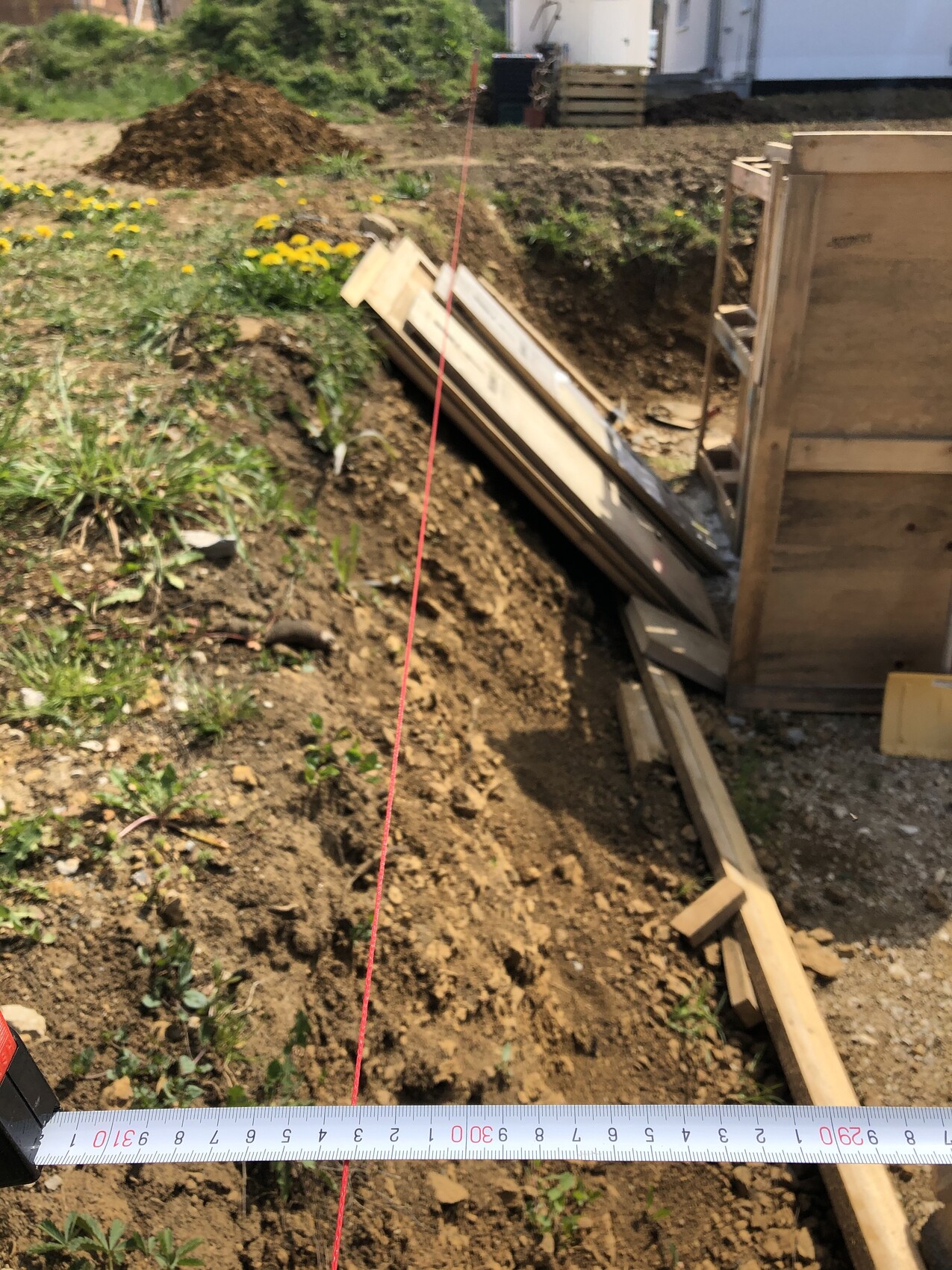 Baustelle: Graben mit Holzformen, rote Schnur als Ausrichtungsmarke, Maßband vorne.