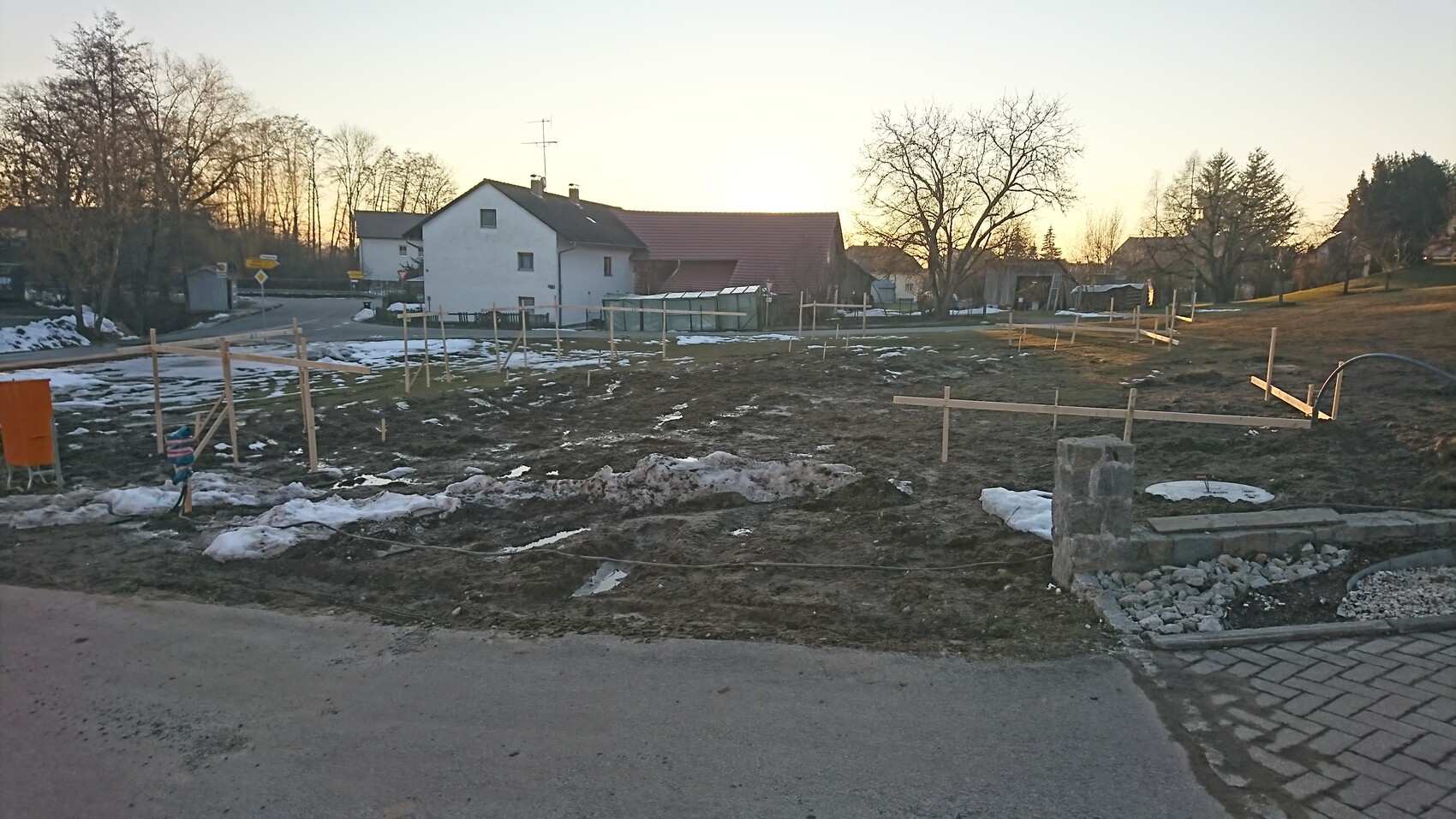 Baustellengelände in einem Wohngebiet mit Holzkonstruktionen, matschigem Boden und Schneeresten.