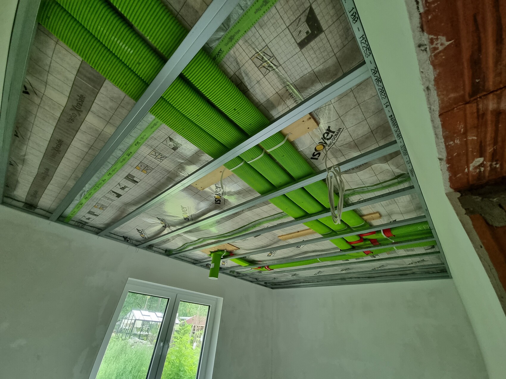 Neubau-Decke: grüne flexible Lüftungsrohre liegen in Metallrahmen, Installationen sichtbar.