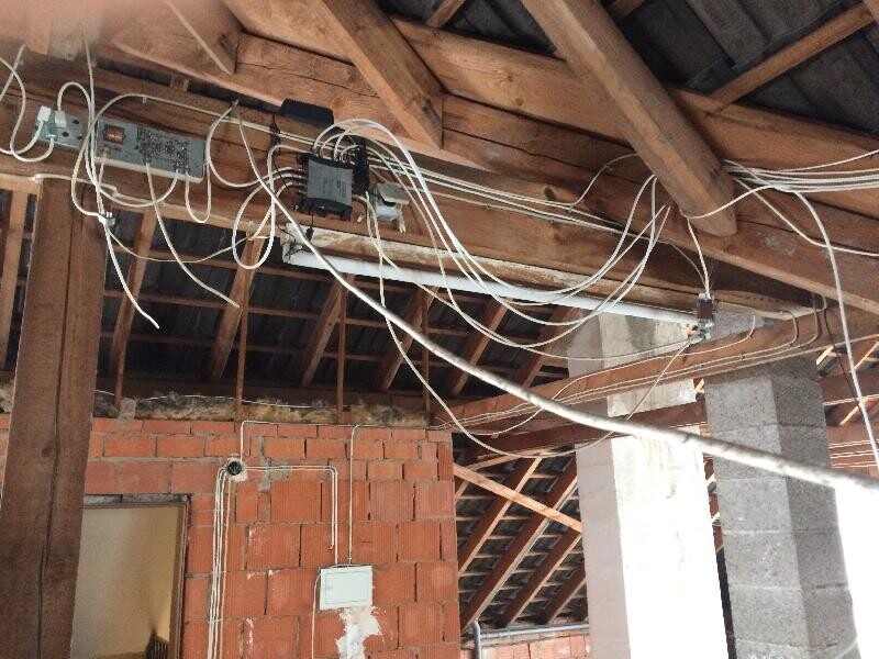 Offener Dachboden mit freiliegenden Kabeln an der Holzbalkendecke über einer Backsteinwand.