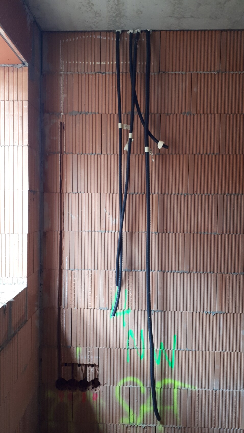 Innenaufnahme eines Rohbaus: freiliegende Ziegelwand, schwarze Kabel hängen von der Decke herab.