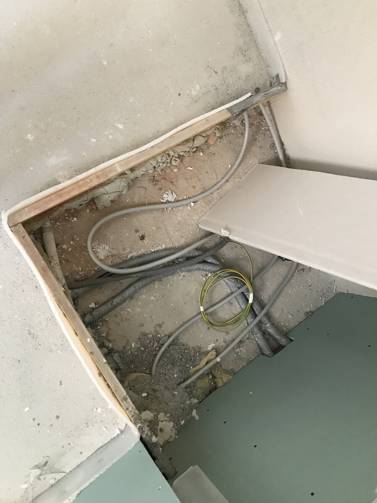 Offene Bauöffnung im Boden mit Kabeln, Rohren, Staub und Holzrahmen.