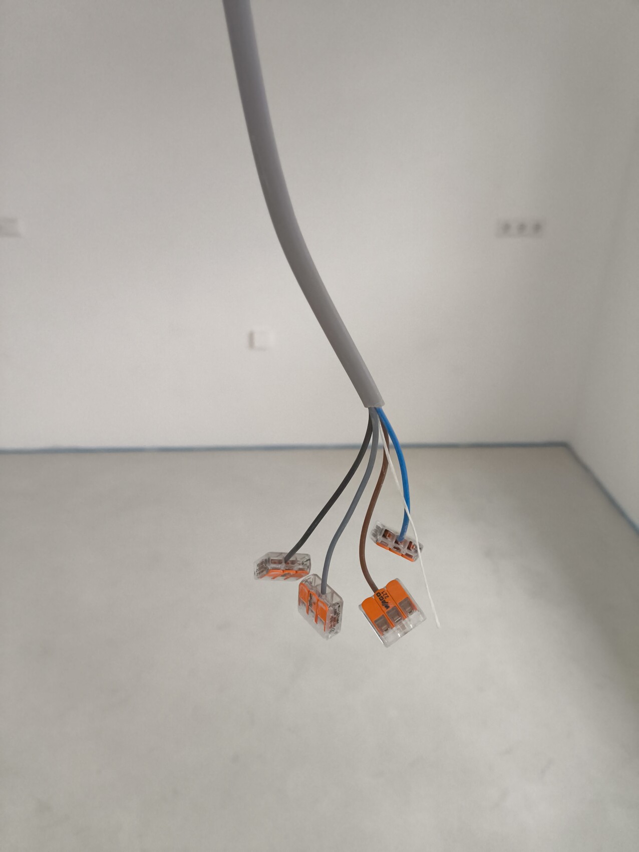 Freigelegte Elektroverkabelung mit mehreren Wago-Steckverbindern in einem leeren, weißen Raum.