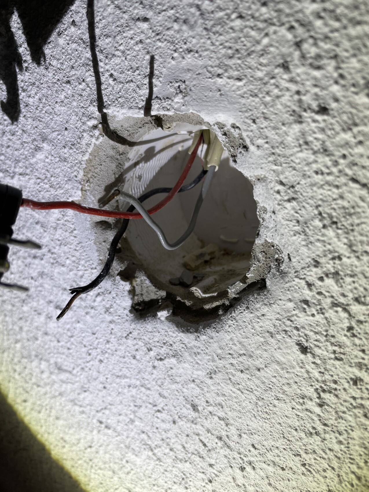 Freigelegte elektrische Kabel in einer Wandöffnung; rotes, schwarzes und graues Kabelbündel.
