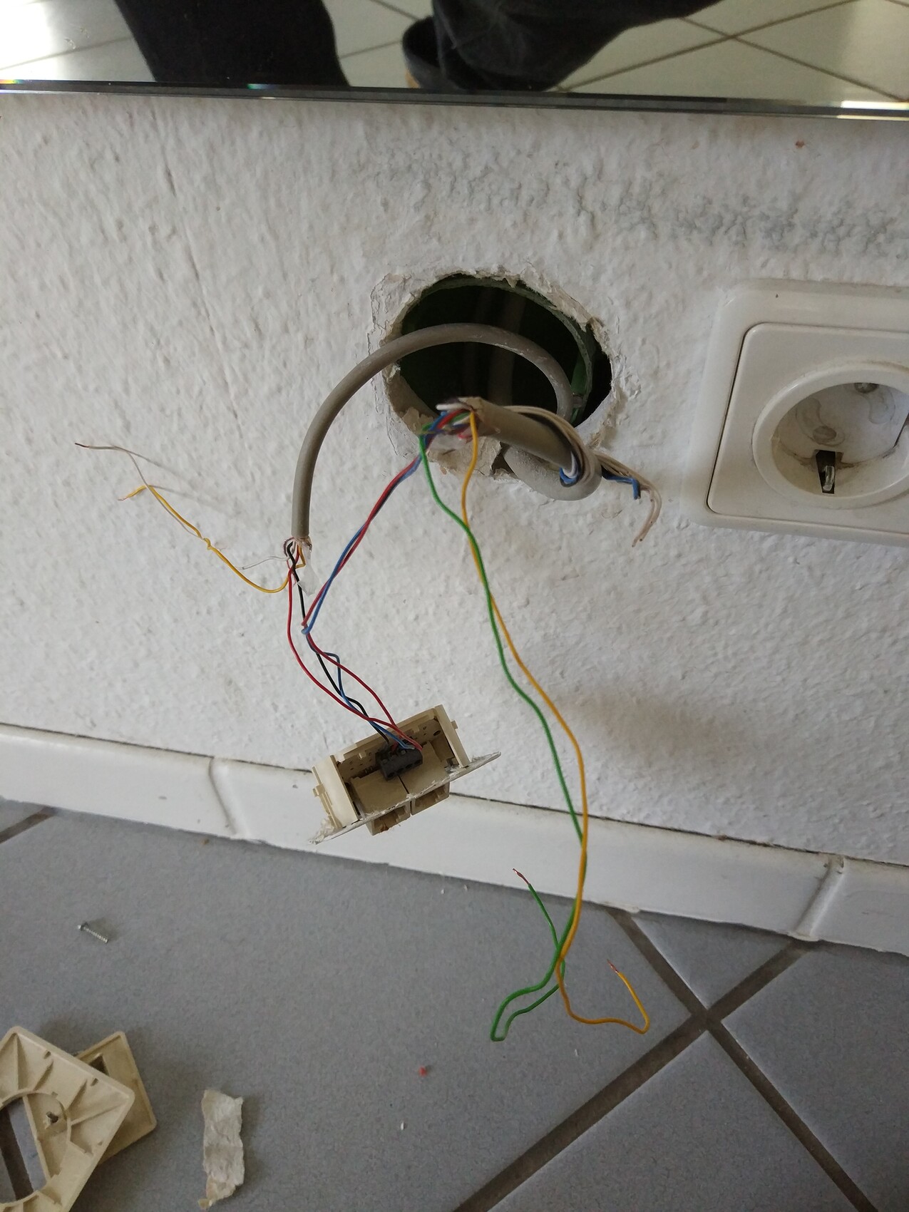 Wandöffnung mit losem bunten Kabelwirrwarr; Kabelreste hängen an Stecker, rechts Steckdose.